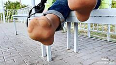 The girl in tan nylons is playing with her feet on the bench