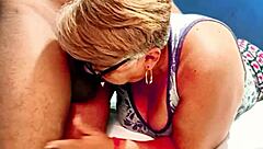 A mature woman with glasses skillfully takes a man's penis in her mouth