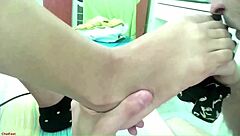 Latina teen couple performs double footjob using dildo socks on bare feet, ending with cum on feet in pov view.