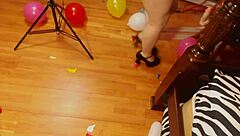 Fifi Foxx playfully pops colorful balloons while strutting in shiny high heels for fun.